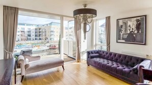 Un salon avec une grande fenêtre, un canapé, un banc et un lustre.