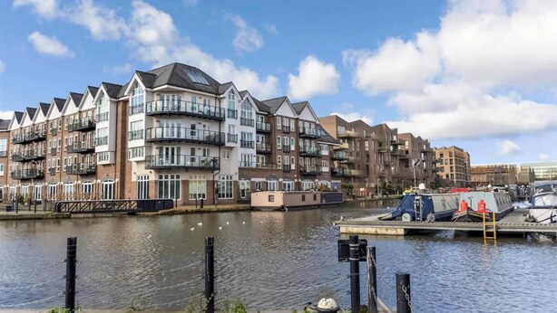 Un immeuble résidentiel situé au bord de l’eau, doté de nombreux balcons, d’un quai avec des bateaux et bordant une rivière paisible.