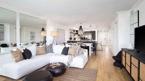 A modern living room with a white sofa, black ottomans, and a dining area in the background. - Dancing Wave, Beachfront, Destin, Holiday Isle (Destin)