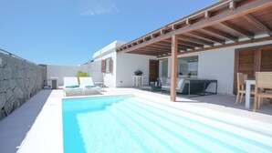 A modern outdoor pool area with a clear blue pool, white lounge chairs, and a wooden pergola.