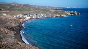 A coastal town with buildings along the shoreline, a clear view of the sea, and a distant mountain range.
