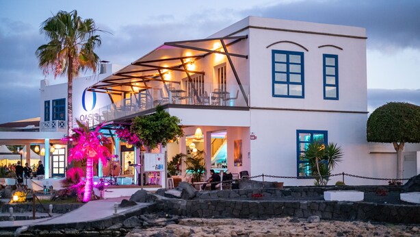 A two-story building with a balcony, a pool, and a palm tree.