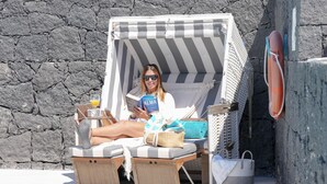 A beachside lounge chair with a striped canopy, a drink, and a book.