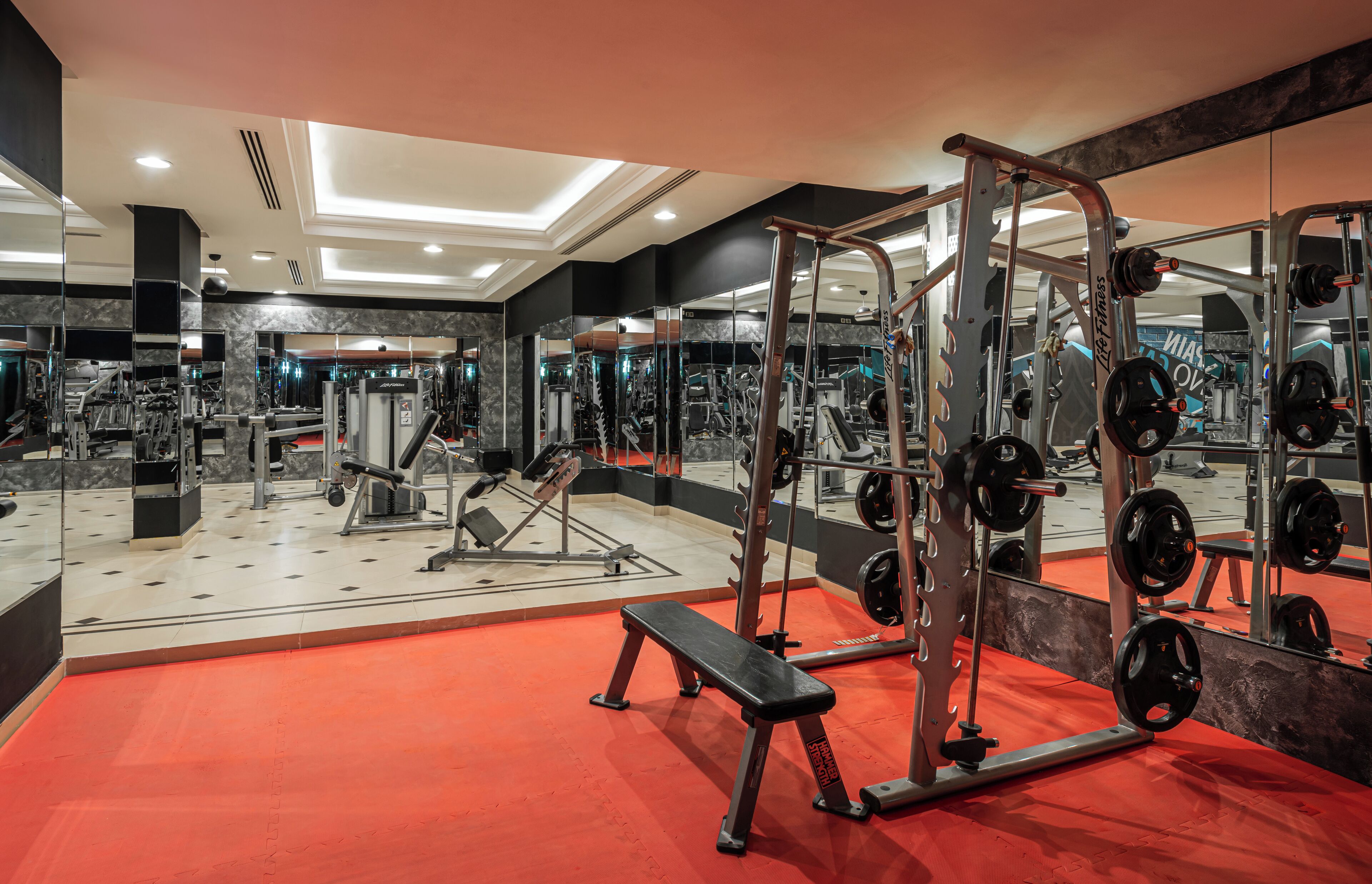 A gym with various exercise equipment, a bench, and a mirrored wall.