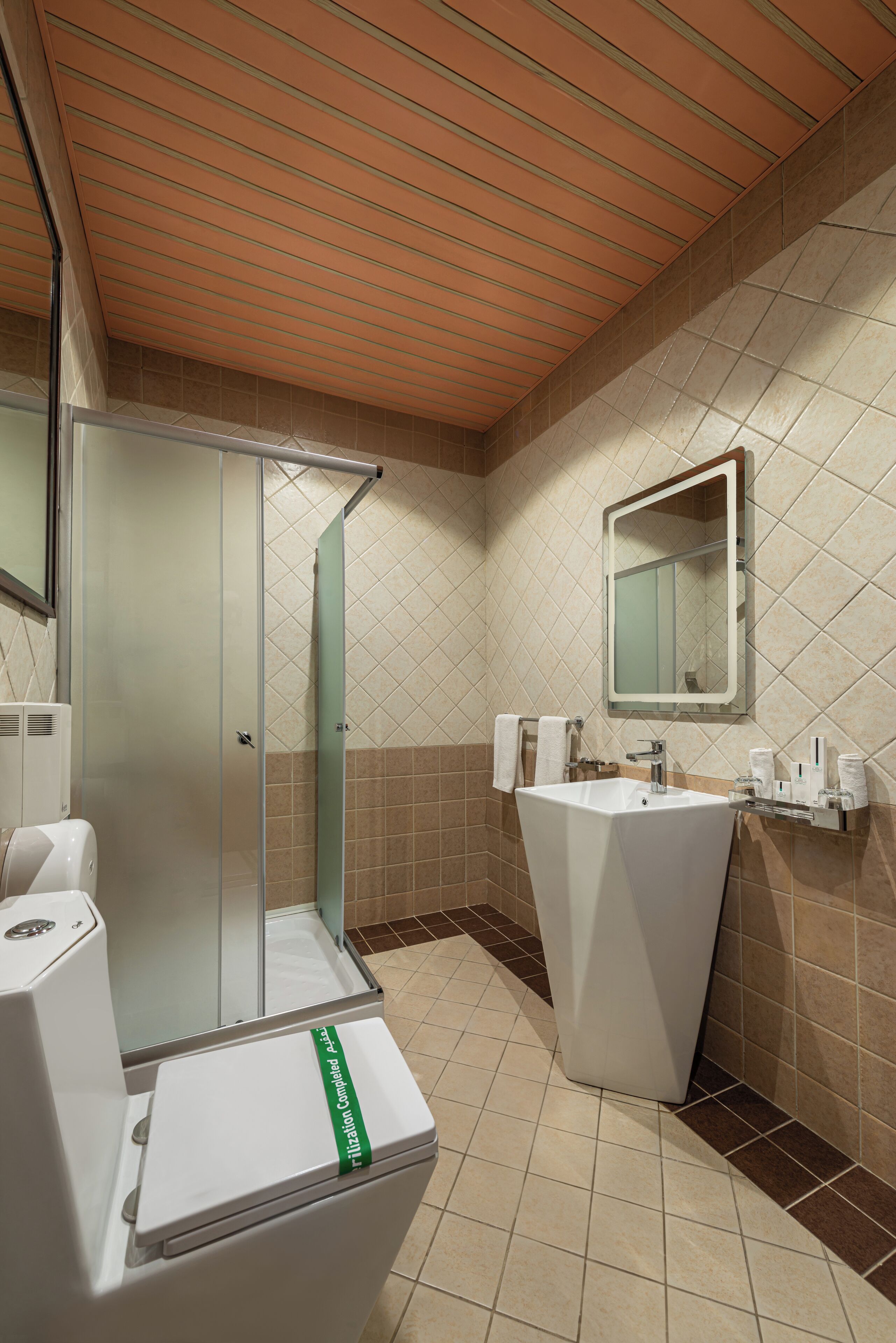 Een badkamer met een douchecabine van glas, een wit wastafeltje en een spiegel erboven.