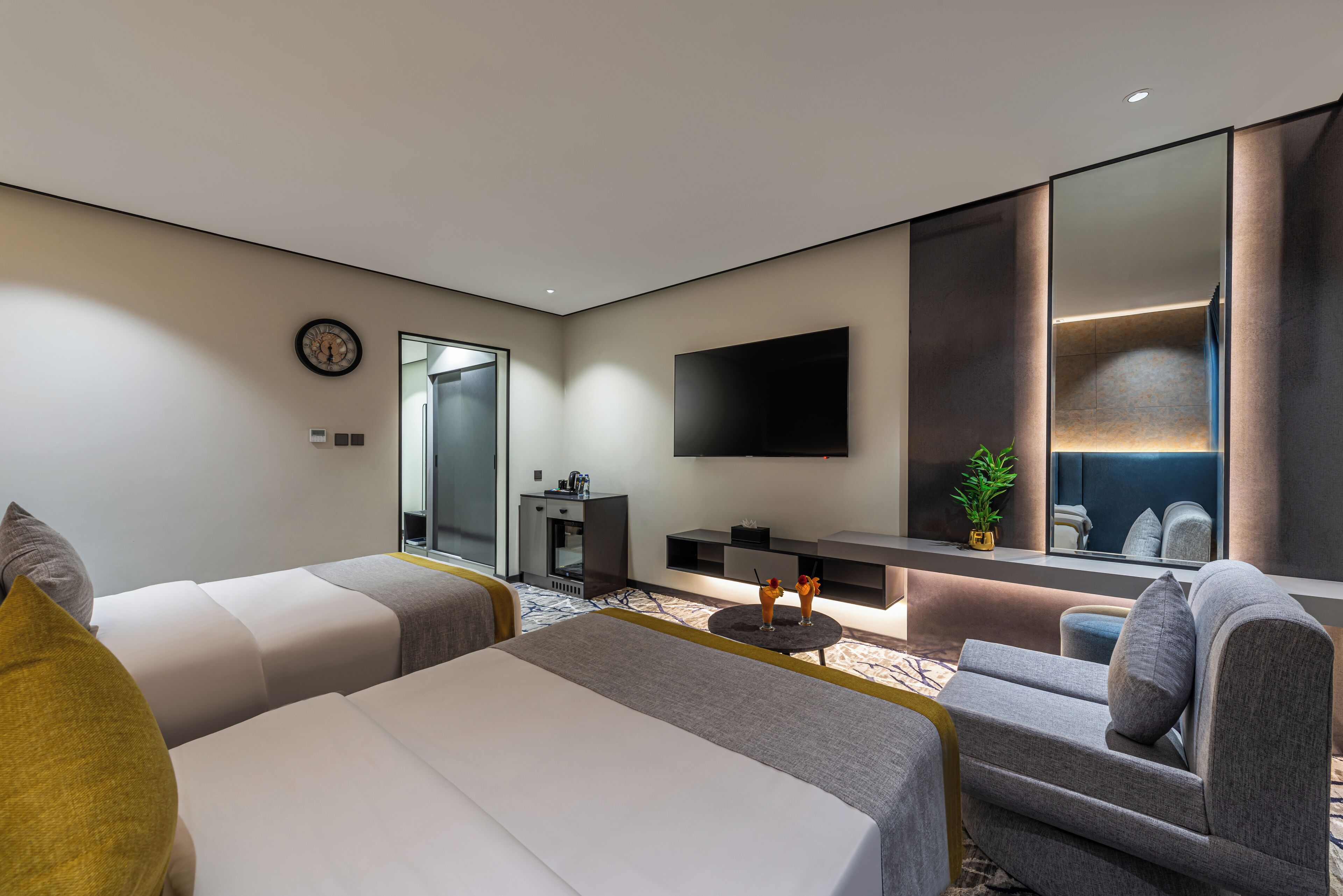 A modern hotel room with a large bed, two sofas, a small table, a TV, and a mirror.
