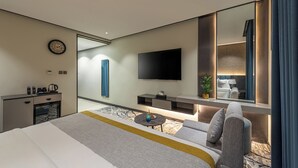 A modern hotel room with a large bed, a flat-screen TV, a desk with a coffee maker, and a seating area with a sofa and armchair. - Ross Hotel  (Riyadh)