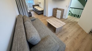 A modern living room with a grey sofa, a wooden coffee table, and a bed with a grey headboard. A TV is mounted on the wall, and there is a staircase leading to an upper level. - Ferienhaus im Altstadtzentrum (Wernigerode)