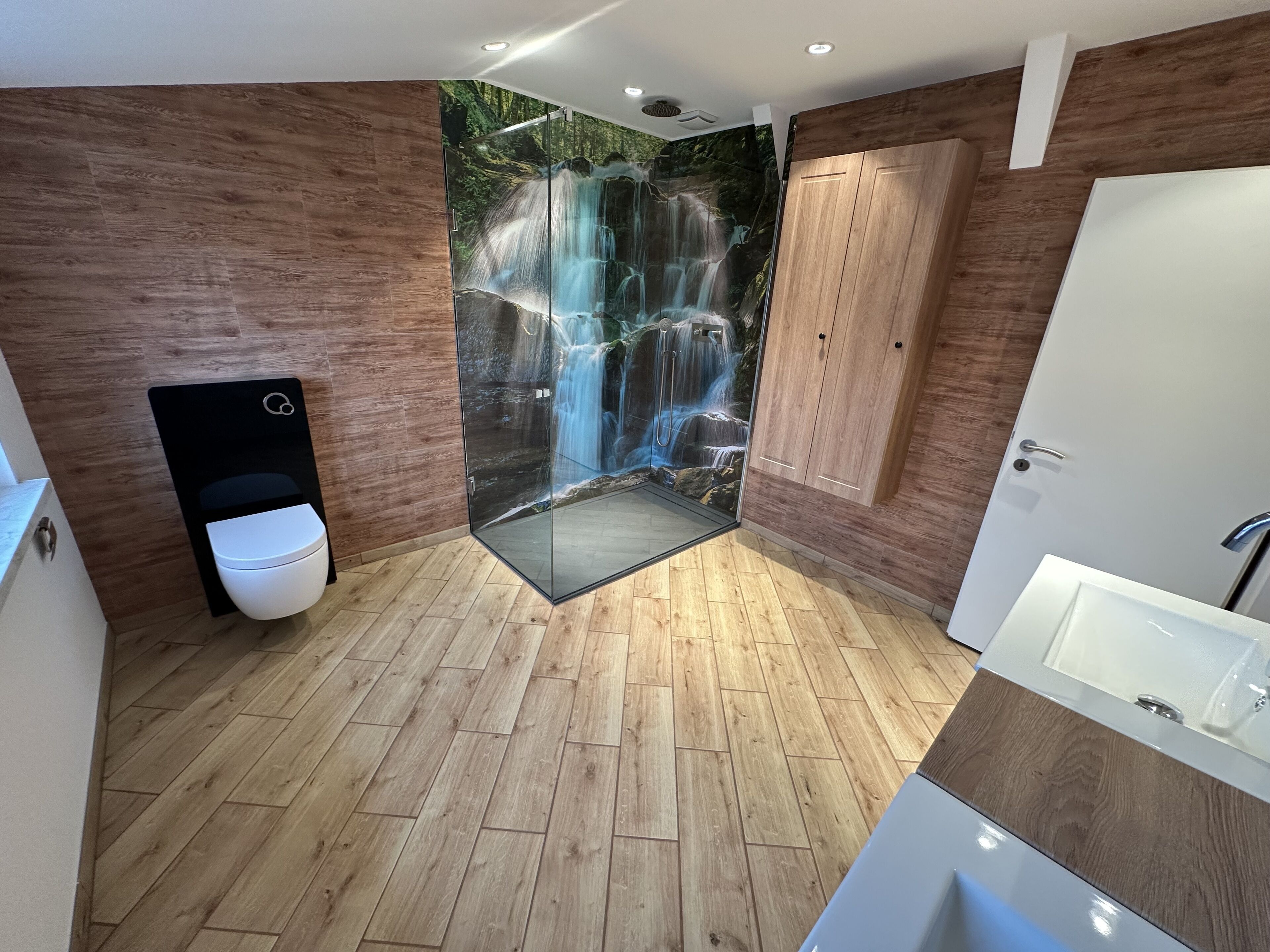 A modern bathroom with a wooden floor, a glass shower enclosure, a toilet, and a bathtub.