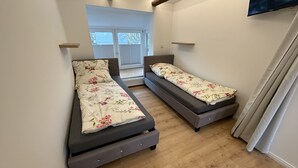 A small, modern room with two single beds, a wooden floor, and a TV mounted on the wall. - Ferienhaus im Altstadtzentrum (Wernigerode)