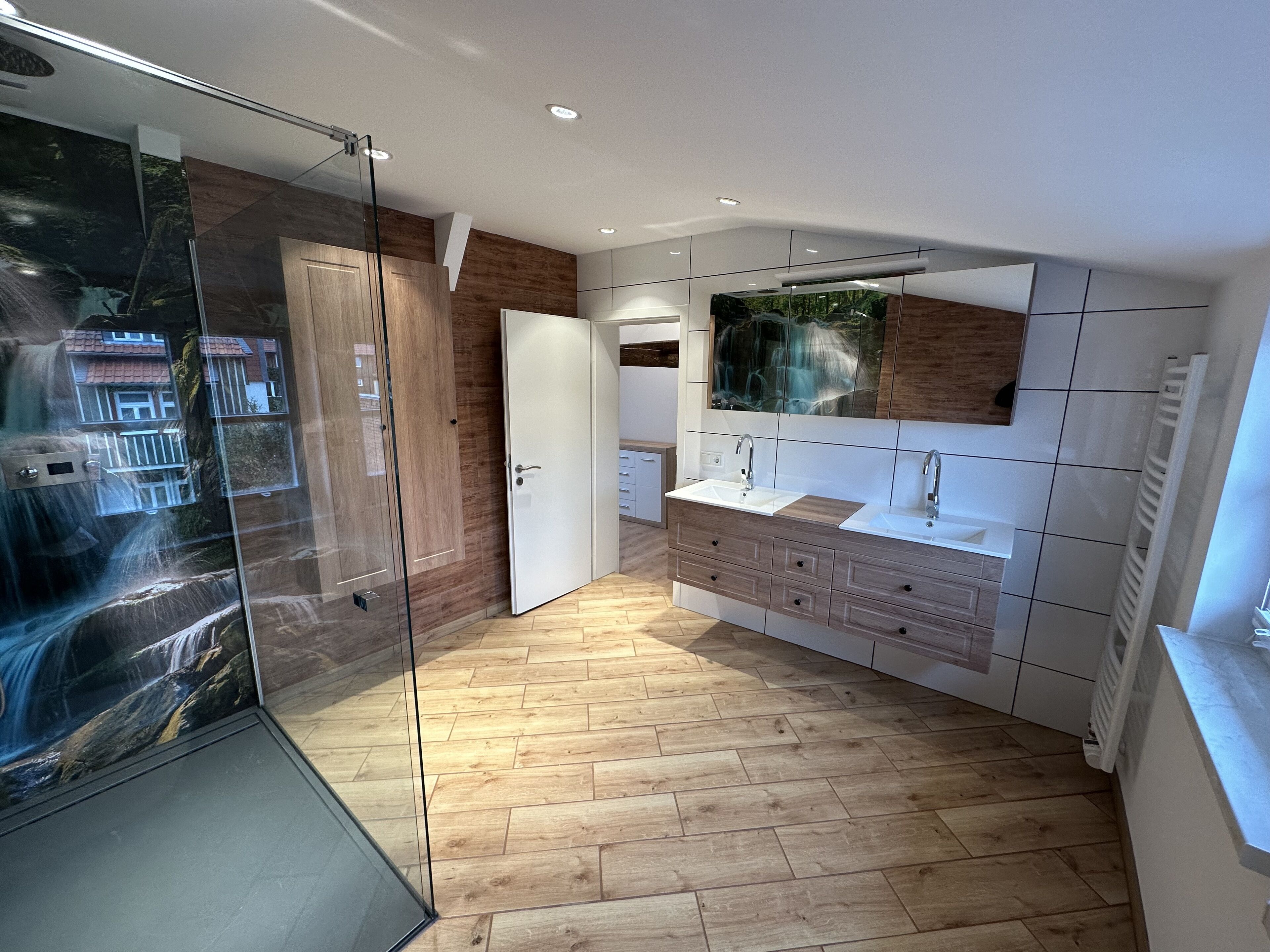 Une salle de bain moderne avec une douche à parois de verre, un plancher en bois et un grand miroir au-dessus du lavabo.
