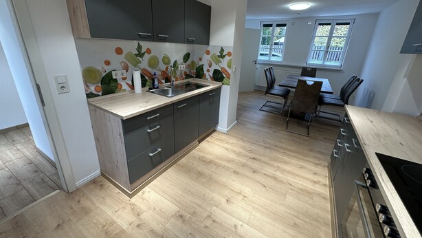 A modern kitchen with dark cabinets, a wooden countertop, and a backsplash with vegetable patterns. There is a dining area with a table and chairs, and a window providing natural light. - Ferienhaus im Altstadtzentrum (Wernigerode)