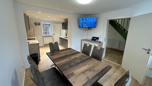 A modern kitchen with a built-in stove, a dining area with a wooden table and chairs, and a TV mounted on the wall. - Ferienhaus im Altstadtzentrum (Wernigerode)