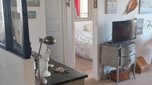 A bedroom with a bed, a desk with a lamp, a television, and artwork on the walls.