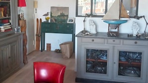 A living room with a red chair, a wooden coffee table, and a desk with a green cabinet.