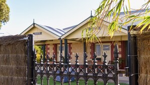 A building with a traditional architectural style, featuring a symmetrical facade, a central entrance with a decorative metal gate, and a pitched roof. - Vineyard Suite for a couple in Historical Homestead, relax on family winery.  (Langhorne Creek)