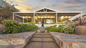A modern building with a covered patio area, stone steps leading to the entrance, and a statue in the center.
