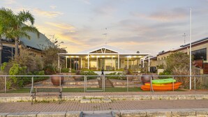 A modern building with a glass facade, surrounded by a landscaped garden with a bench and kayaks.