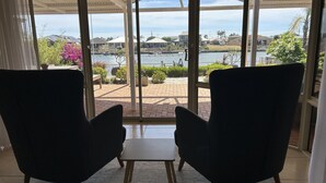 A room with two armchairs facing a large window overlooking a patio area with a view of a body of water and distant buildings.