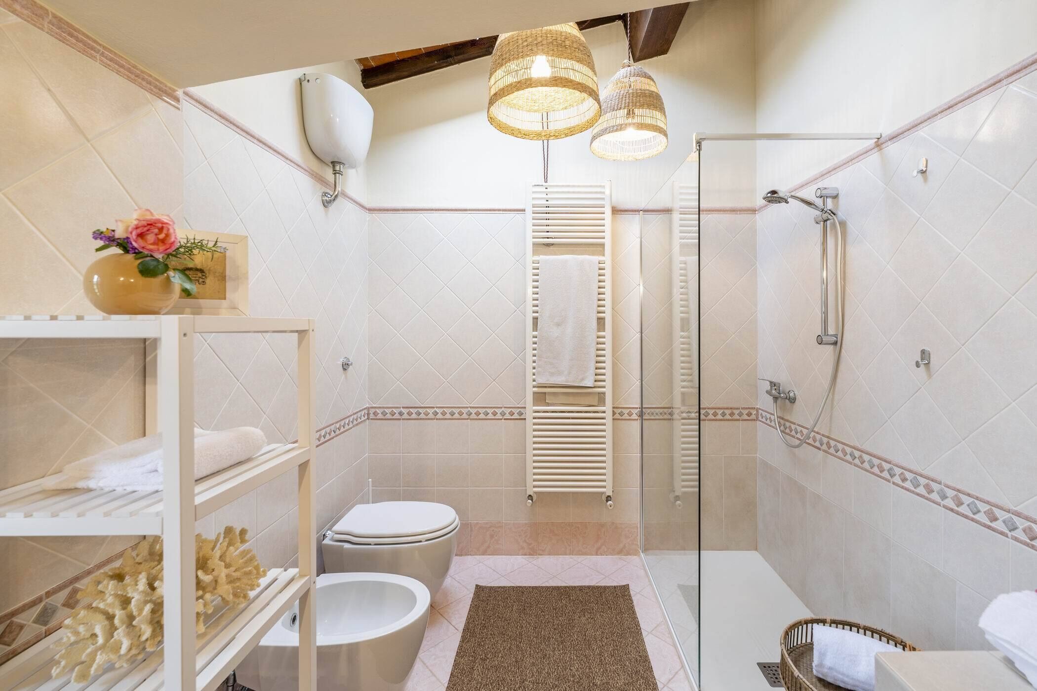 Un baño moderno con cabina de ducha de vidrio, inodoro, lavabo y estante con toallas y un florero.