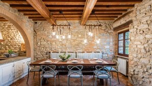 A stone-walled dining area with a wooden table set for four, surrounded by metal chairs. - Charming villa in Chianni,Pool,garden, A/C, Pergola for al fresco dining,sleep 9 (Chianni)