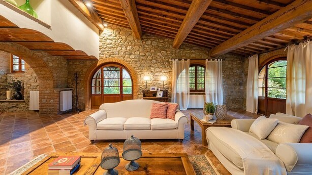 A cozy living room with stone walls, wooden beams, and a large arched window. - Charming villa in Chianni,Pool,garden, A/C, Pergola for al fresco dining,sleep 9 (Chianni)
