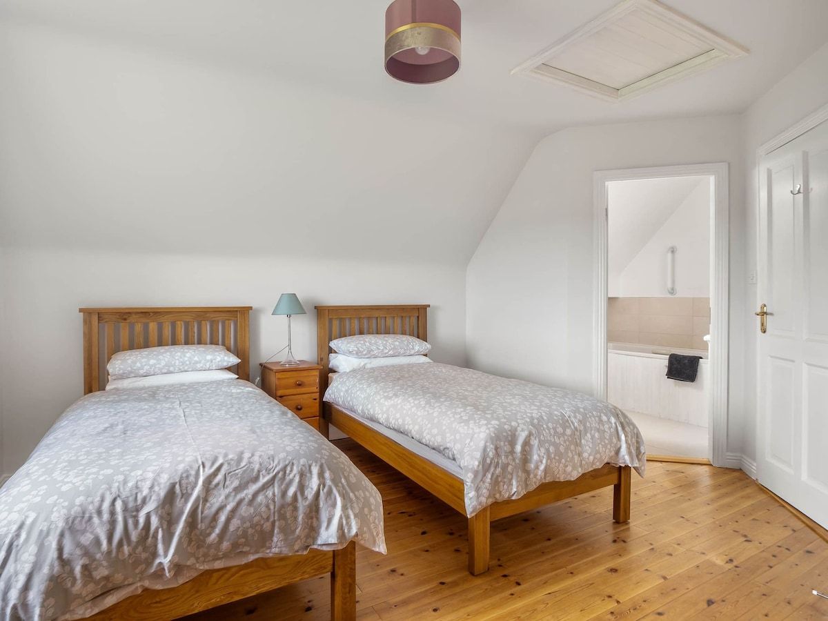 A bedroom with two wooden beds, a nightstand with a lamp, and a white door leading to a bathroom.