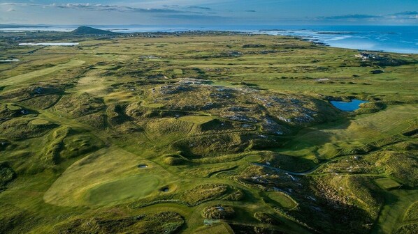 An aerial view of a golf course with multiple holes, water bodies, and a distant mountain.