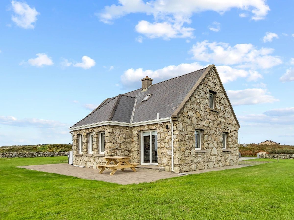 A stone house with a pitched roof, a front door, and a picnic table outside.