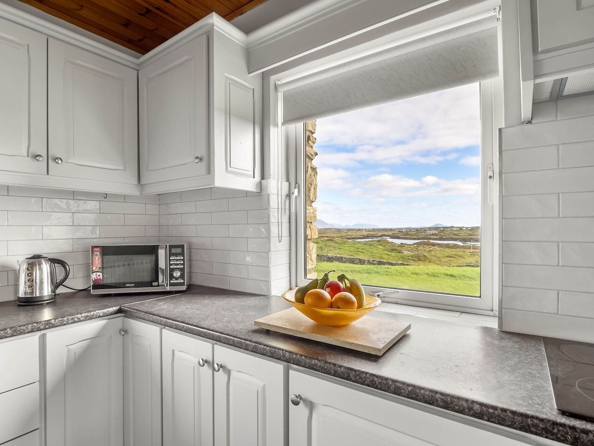 A kitchen with white cabinets, a microwave, and a bowl of fruit on the counter.