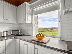A kitchen with white cabinets, a microwave, a kettle, and a bowl of fruit on the counter.