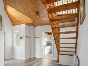 A spacious room with a wooden ceiling, a staircase, and a kitchen visible through an open door. - Lake House Mannin, Ballyconneely (Ballyconneely)