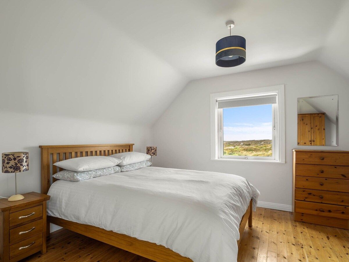 Un dormitorio con cama, cómoda de madera, mesita de noche y ventana con vistas.
