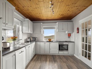 A kitchen with white cabinets, a wooden ceiling, a window, and a view of the outdoors.