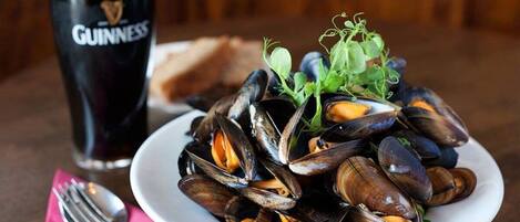 A plate of mussels with a glass of Guinness beer and a fork on a table.