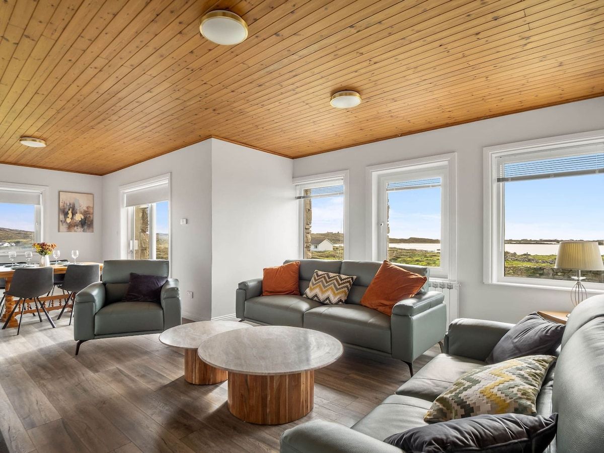 Un espacio habitable amplio con techo de madera, ventanas grandes y vistas al paisaje.