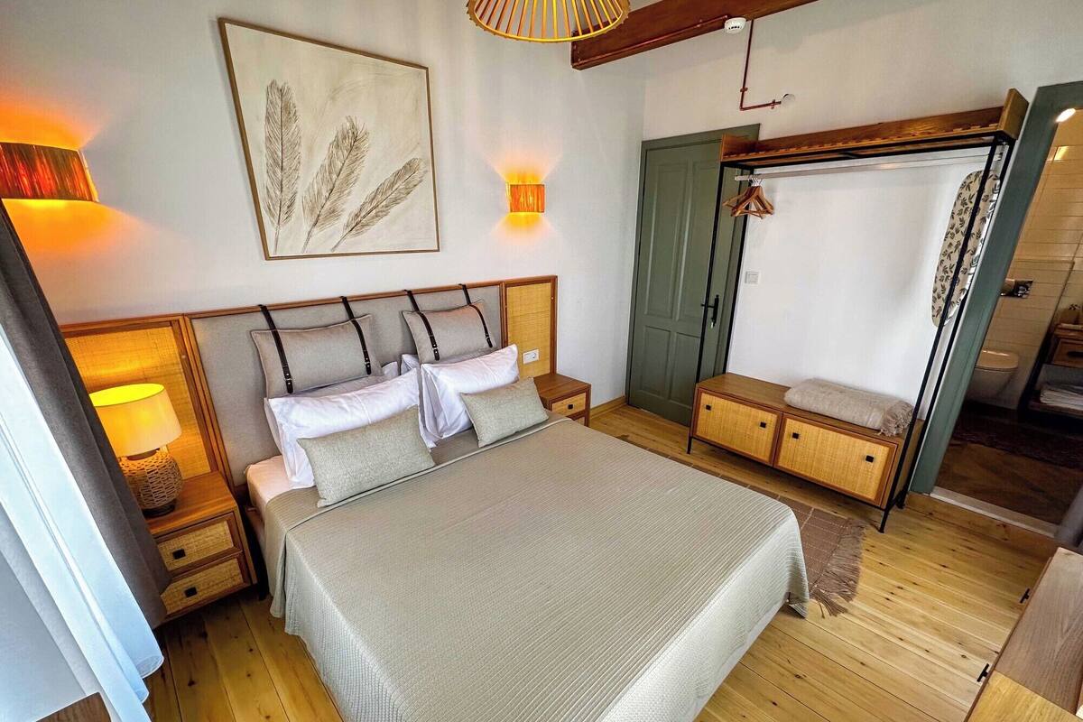 A bedroom with a bed, bedside tables, a wardrobe, a hanging clothes rack, and a painting on the wall.
