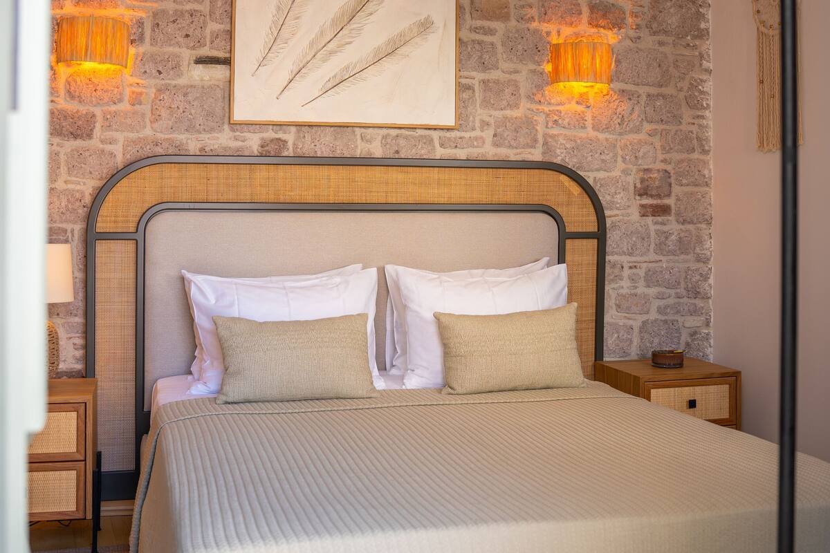 A bedroom with a large bed, a stone wall, and a hanging light fixture.