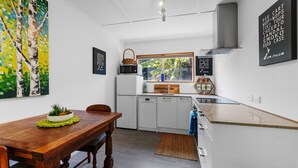 Une cuisine moderne avec des meubles blancs, une table à manger en bois et une grande fenêtre donnant sur un paysage verdoyant.