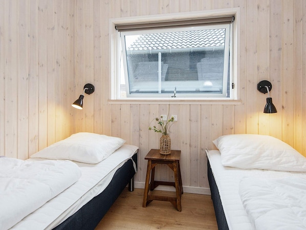 A room with two beds, a window with a view, and two wall-mounted lamps.