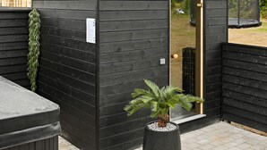 Une structure en bois de couleur noire, dotée d’une porte, d’une petite fenêtre et d’une plante en pot placée devant.