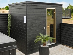 A black wooden structure with a door, a small window, and a potted plant in front.