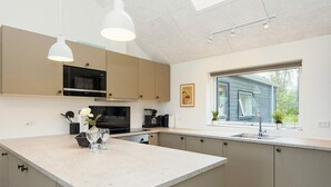 Une cuisine moderne dotée d’un îlot central, d’appareils électroménagers en acier inoxydable et d’une fenêtre offrant une vue sur l’extérieur.