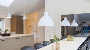 Une cuisine moderne avec une longue table à manger, des luminaires suspendus blancs et une vue sur l’extérieur.