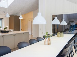 A modern kitchen with a long dining table, white pendant lights, and a view of the outside.