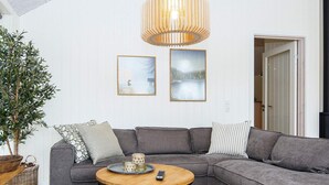 Un salon moderne avec un canapé d’angle gris, une table basse ronde en bois et une plante en pot.