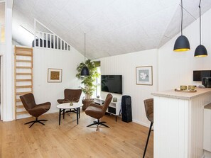 A modern living space with a staircase, a dining area with chairs and a table, a TV, and a kitchen counter.