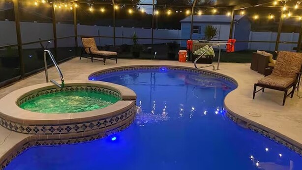 Una piscina amb una banyera d'hidromassatge, envoltada de cadires i llums penjants.