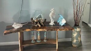 Una taula de consola de fusta amb objectes decoratius i un vas, col·locada en una habitació amb un televisor de pantalla plana muntat a la paret.