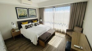 A hotel room with a bed, bedside table, bench, and a desk.